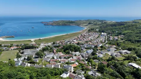 BBC An aerial view over a small town on an island, with a sweeping sandy bay behind.