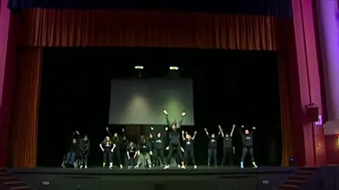 Dance troupe on state with their arms in the air