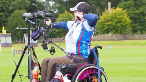 Support Dogs A woman in a wheelchair playing archery
