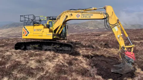 A digger presses down the exposed area of brown peat on an open moorland