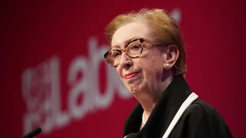 Dame Margaret Beckett stands in front of a Labour party logo