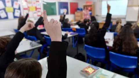 Getty Images Children raising their hands in a classroom