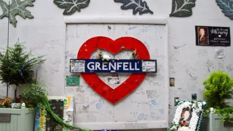Getty Images Tributes are seen on the Grenfell Tower memorial wall as the inquiry report is published.