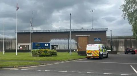PA Media A police van is parked outside a low flat-roofed building with a plaque reading 'HMP Frankland' on the wall