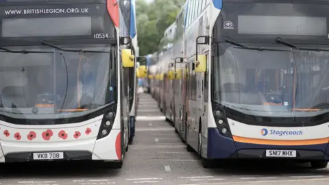 Getty Images Two Stagecoach branded double decker buses parked side by side, one also decorated with pictures of Remembrance Day poppies.